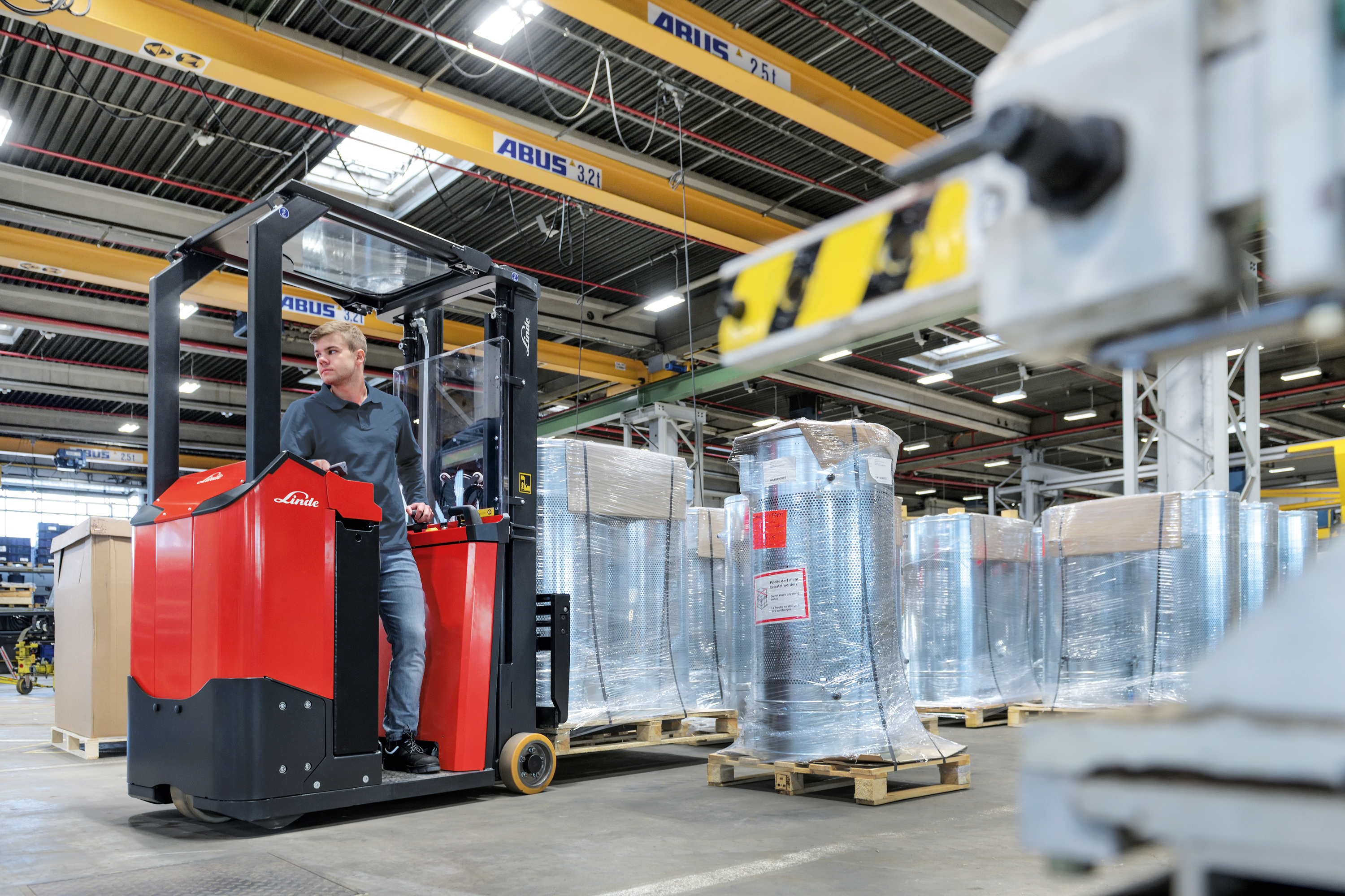 Compacte elektrische driewiel heftruck bestuurt door medewerker in magazijn - Rijdt achteruit - Hefvermogen van 1 ton