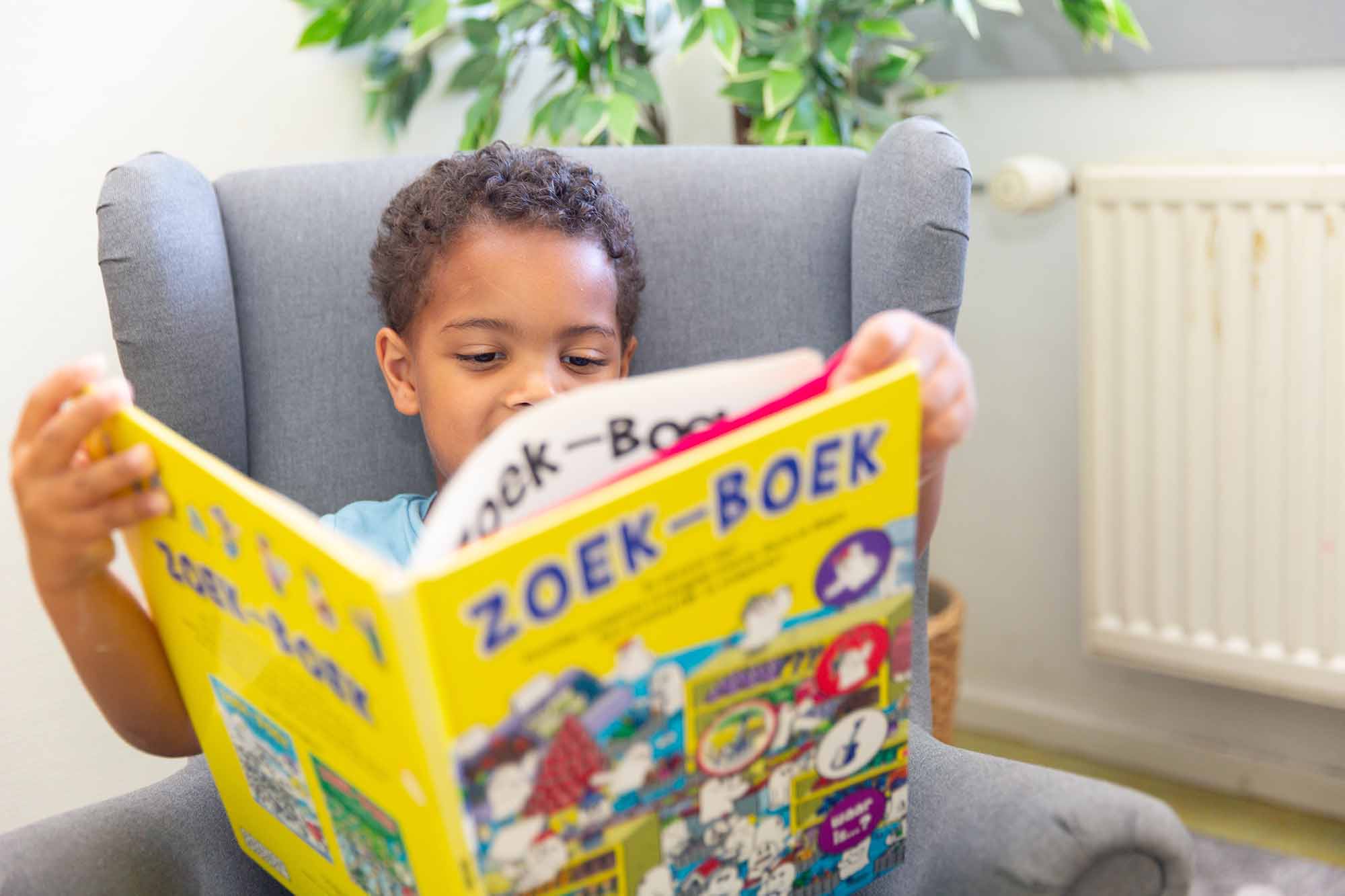 Jongen zit in een fauteuil en leest een boek. 