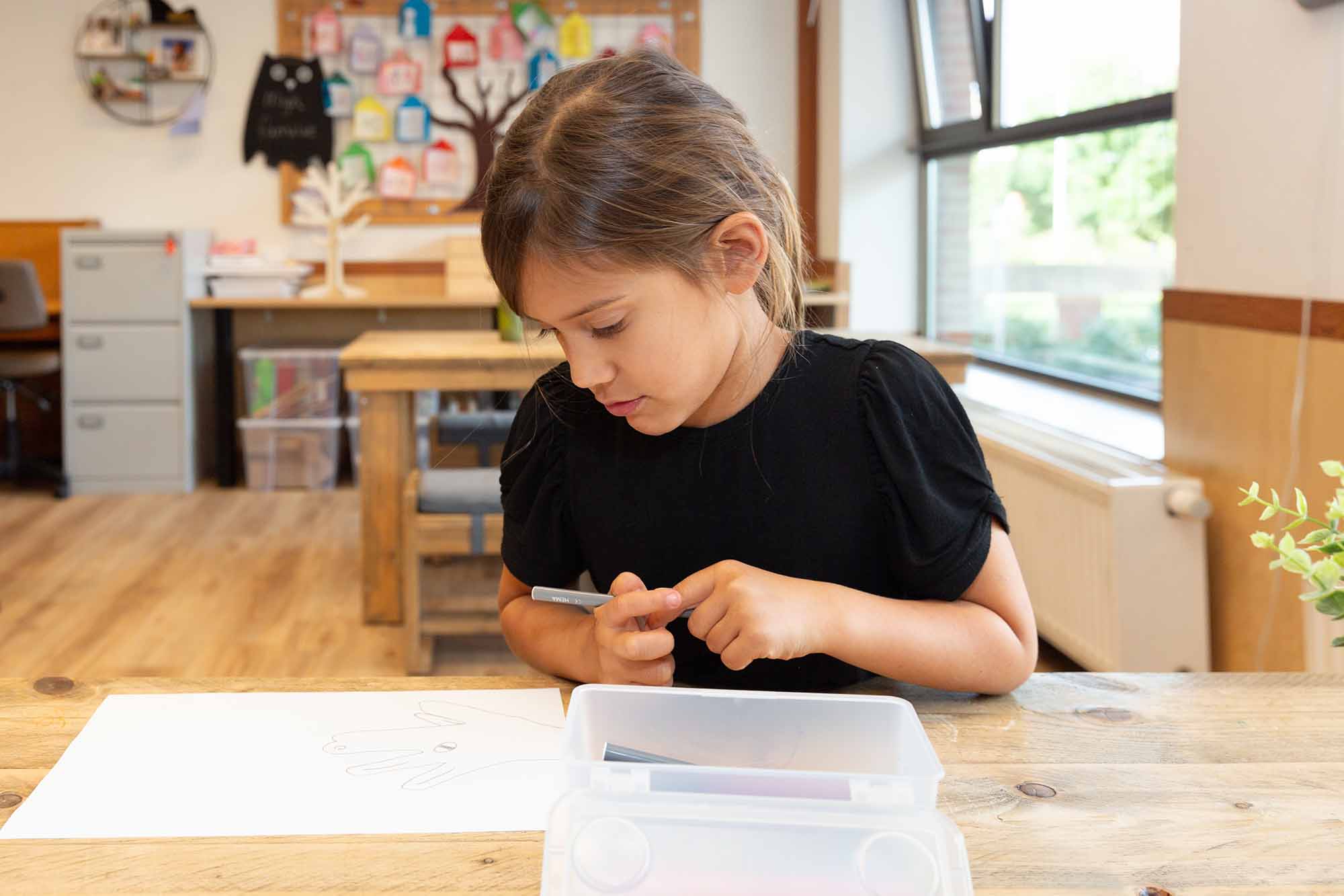 Meisje maakt tekening van hand aan tafel van kinderopvang locatie.