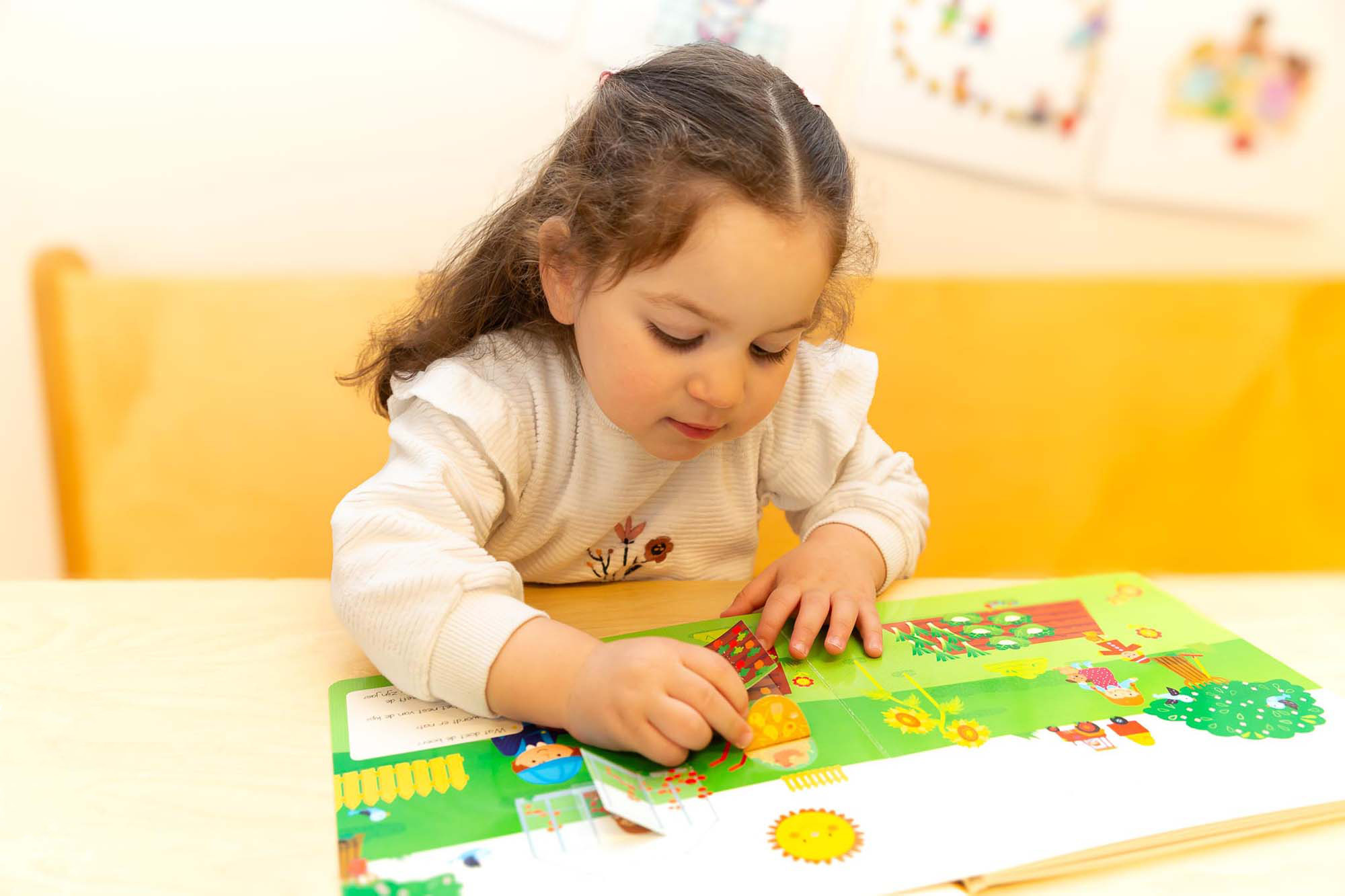 Peuter speelt met boekje en maakt vakjes open aan tafel van kinderopvang locatie.